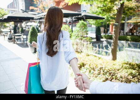 Torna l'aspetto di una donna con le borse della spesa tirando una mano di un uomo al di fuori Foto Stock