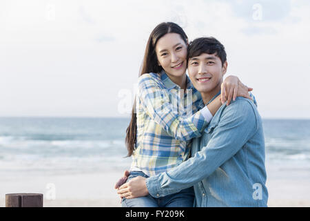 Matura in abbraccio con lo sguardo in avanti con un sorriso in spiaggia Foto Stock