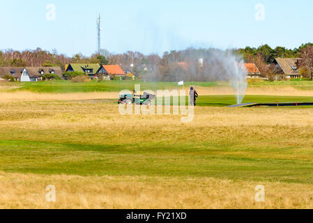 Skanor, Svezia - 11 Aprile 2016: lavoratore di sesso maschile di irrigazione è sul campo da golf ma il flessibile dell'acqua perde e diffondere l'acqua fino a Foto Stock