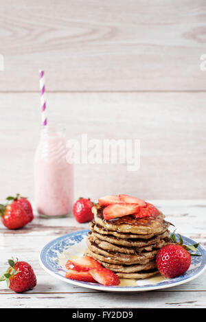 Pila di sano carburatori bassa oat e banana pancake bianco su sfondo di legno. Latte di fragola e fragole fresche Foto Stock