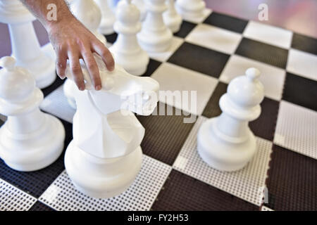 Mano spostando il pedone nero su una scacchiera gigante Foto Stock