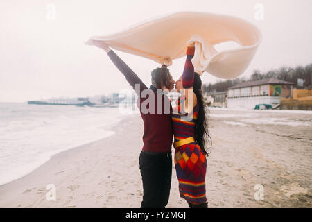 Attraente giovane coppia felice baciare sotto coltre bianca sulla spiaggia invernale. Concetto vintage Foto Stock
