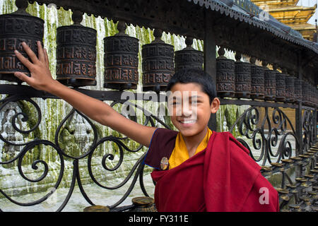 Buddista Tibetana giovane monaco a piedi dalle ruote della preghiera e bandiere a Swayambhunath o Tempio delle Scimmie, Kathmandu, Nepal Foto Stock