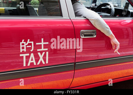 Red Hong Kong taxi, ruota sul lato destro, driver la mano con la sigaretta fuori dalla finestra, Hong Kong, Cina Foto Stock