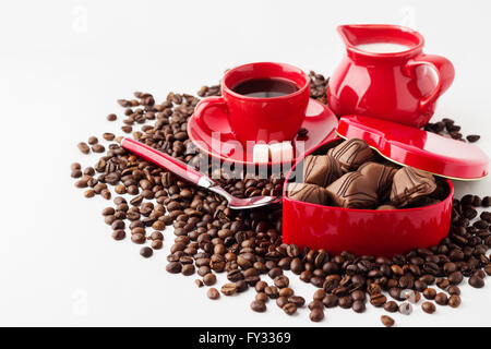 Tazza di caffè, latte e una scatola (a forma di cuore) con cioccolatini sui chicchi di caffè. Isolato su sfondo bianco. Foto Stock