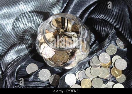 Flaconcino di vetro con shine monete e nei pressi di denaro sul giorno nero Foto Stock