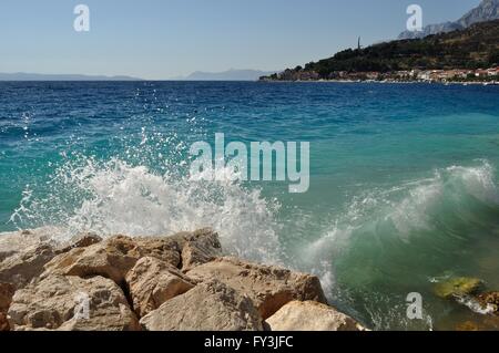 Onde sulla bellissima spiaggia con pietre in podgora. in background con il monte Biokovo e il monumento del gabbiano ali. Croazia Foto Stock