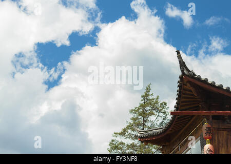 Cinese tradizionale tetto curvo (spazzamento curvatura) con lanterne rosse contro il cielo nuvoloso della provincia dello Yunnan Foto Stock