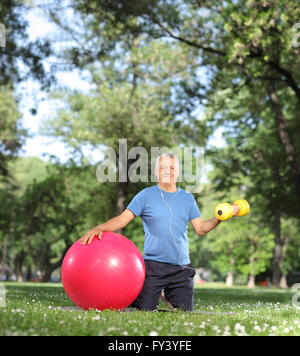 Uomo maturo che esercitano nel parco con un manubrio di colore giallo e una palla fitness shot con inclinazione e spostamento lente Foto Stock