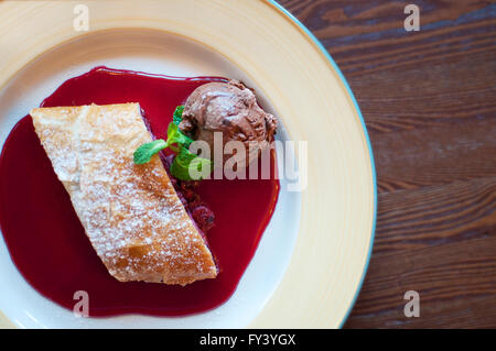 Piastra con strudel di ciliegie, sciroppo e una pallina di gelato al cioccolato Foto Stock