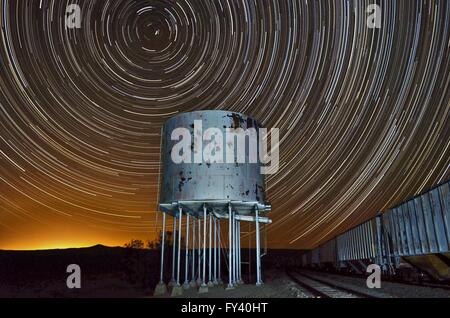 Star trail con la vecchia ferrovia water tower e vagoni ferroviari. Le stelle si formano un modello circolare nel cielo notturno sopra la torre dell'acqua. Foto Stock