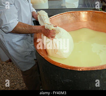 Pastore casaro raccoglie il formaggio dal grande paiolo di rame con il latte di vacca e latte di capra Foto Stock