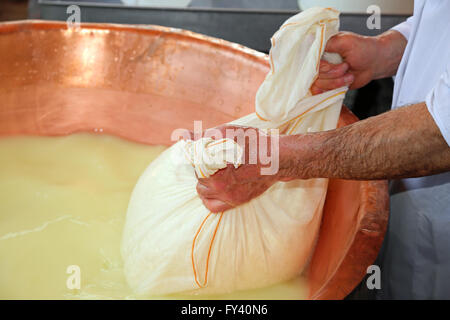 Pastore casaro raccoglie il formaggio dal grande paiolo di rame con il latte di vacca e latte di capra Foto Stock