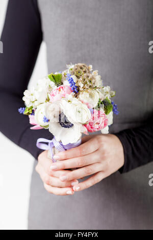Donna in abito grigio e camicia nera è in possesso di una molla bouquet di tulipani rosa, viola uva giacinti, anemoni bianchi, viola Foto Stock