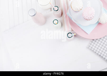 Quattro bottiglie di frappè, tre con cannucce e bicchiere di latte e le piastre con rosa e bianco meringhe e panno sul legno bianco Foto Stock