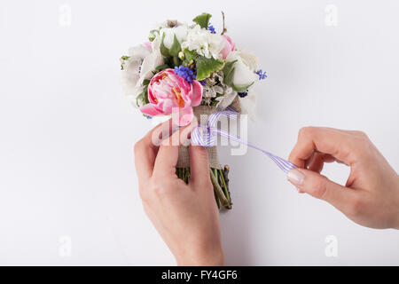 Le due mani sono la realizzazione di un arco a partire da un nastro violaceo nella splendida primavera bouquet di tulipani rosa, viola uva giacinti, un bianco Foto Stock