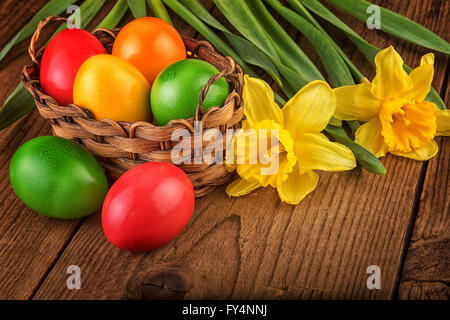 Colorate decorazioni di pasqua con le uova nel paniere scuro su un tavolo di legno. Foto Stock