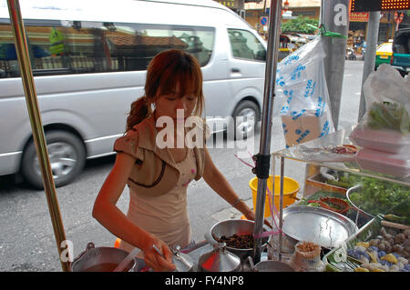 Cucina di strada venditore prepara i suoi piatti come il traffico ruggisce da a Bangkok, in Thailandia Foto Stock