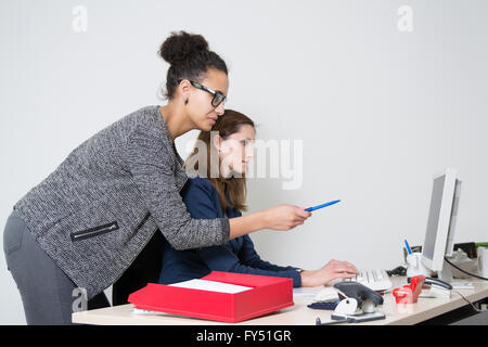 Due donne di business nella parte anteriore del computer in ufficio. Entrambe le donne stanno cercando di monitor. Una donna è rivolta a m Foto Stock