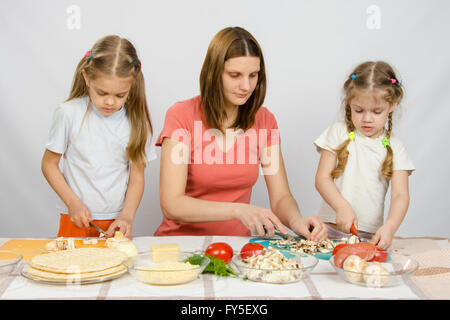 La mamma insegna due figlie di cucinare. Li aiuta a tagliare i funghi e verdure Foto Stock