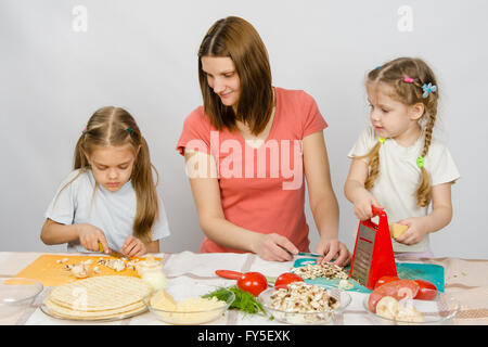 La mamma con cinque anni di figlia guardato come la figlia maggiore di taglio pizza funghi Foto Stock