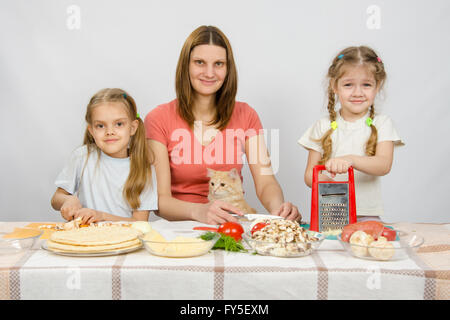 Madre e due bambine a un tavolo preparato gli ingredienti per la pizza. Essi sono stati a guardare un gatto Foto Stock