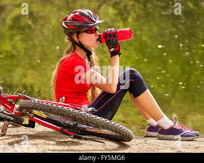 Bike bicicletta bambina indossa un casco. Ragazza in bicicletta di bere acqua in bottiglia. Foto Stock