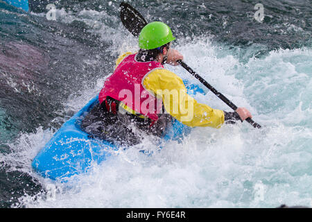 Giovane uomo maschio canoa kayak in acqua bianca. Egli paddling veloce per scendere le rapide. Egli indossa luminoso abbigliamento colorato Foto Stock