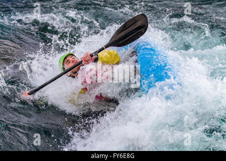 Giovane uomo che sta per andare sotto l'acqua nel suo kayak , che tiene in mano la racchetta e acqua è fluente e la preparazione di schiuma di tutti intorno alla barca. Foto Stock