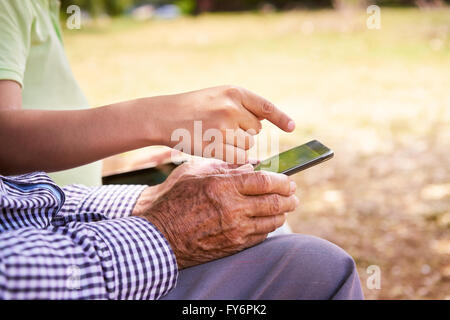 Uomo Senior learning internet e telefoni cellulari: bambino aiutando il suo nonno navigare sul web con il suo nuovo telefono cellulare. Primo piano Foto Stock