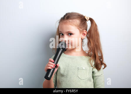 Carino fun kid ragazza cantare canzone nel microfono su sfondo blu. Giovani talenti Foto Stock