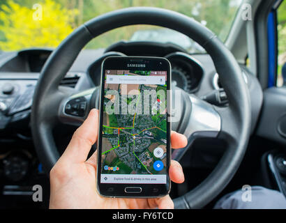 Close-up di una mano che tiene un telefono con le mappe di Google app aperta all'interno di una Ford Fiesta auto. Foto Stock
