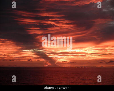 Drammatica in rosso e arancione luce splende attraverso le nuvole come i tramonti sull'oceano pacifico Foto Stock