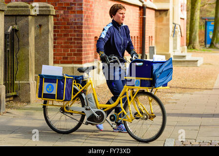 Trelleborg, Svezia . Aprile 12, 2016: Femmina mailman spingendo una bicicletta piena di mail e lettere lungo il marciapiede. Foto Stock