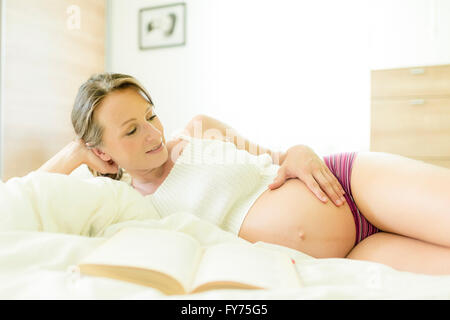 Donna incinta giacente a letto Foto Stock