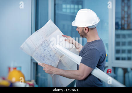 Ritratto di un architetto builder studiando piano di disposizione delle camere, serio ingegnere civile che lavora con i documenti Foto Stock