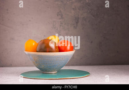 Ancora in vita con i pomodori nella ciotola sul tavolo della cucina è un mix di pomodoro con diversi colori muro di pietra lo sfondo con copia Foto Stock