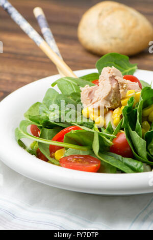 Spinaci freschi con insalata di tonno e mais, piccoli pezzi di pomodori ciliegia in piastra bianca sul tavolo di legno Foto Stock