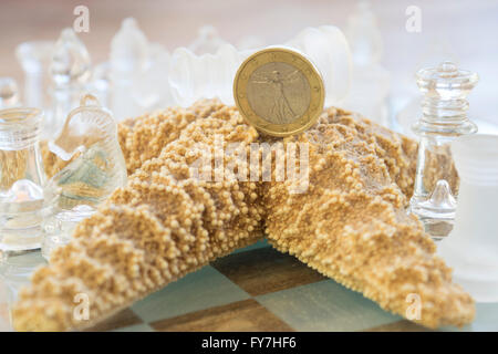 Un euro su una stella di mare tra i pezzi di una scacchiera di vetro Foto Stock