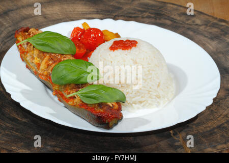 Zucchine ripiene, riso, stufati di peperoni e pomodori, verdura, il lato piatto e guarnite con foglie di basilico su una piastra Foto Stock