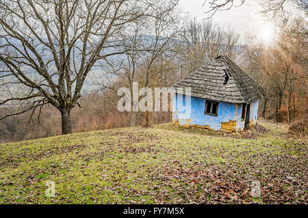 Rovinato blue vecchia casa fatta di argilla in collina circondata da alberi. Foto Stock