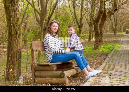 Bella donna incinta all'aperto con il suo bambino nel parco sul banco di lavoro. Foto Stock