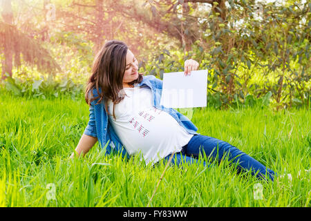 Bella donna incinta all'aperto con una carta in mano che mostra il giorno della nascita del suo bambino. Foto Stock