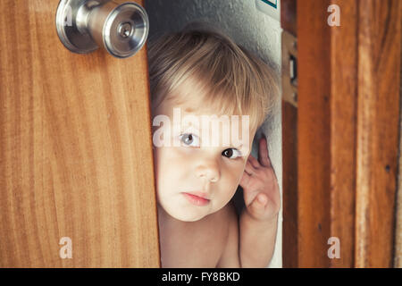 Poco bionda caucasica baby apre la porta e guarda al di fuori Foto Stock