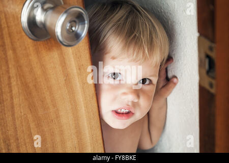 Poco bionda caucasica Baby girl apre la porta e guarda al di fuori Foto Stock