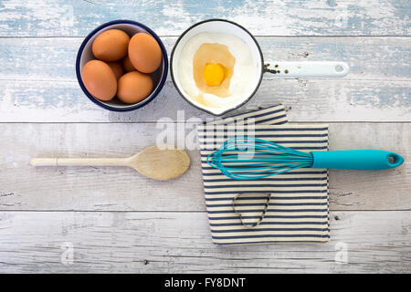 Le uova in una terrina con una frusta su una tavola in legno rustico top shot dal di sopra Foto Stock