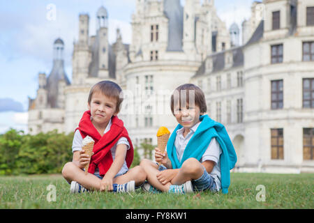 Due ragazzi adorabili in abbigliamento casual, mangiare il gelato seduto su un prato di fronte al più grande castello lungo il fiume Loira, C Foto Stock