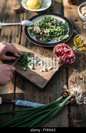 La preparazione di insalata verde con melograno, manna groppa e cipollina, tritare la cipolla a molla Foto Stock