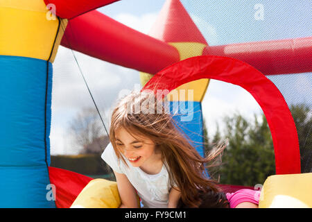 Ragazza giovane giocando su un castello gonfiabile in giardino Foto Stock