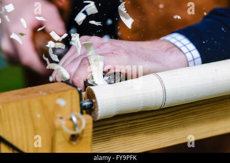 I trucioli volano dal bordo di un cesello di legno come un uomo diventa di legno su un tornio. Foto Stock